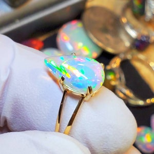 May include: A gold ring with a pear-shaped opal gemstone. The opal is iridescent with shades of green, blue, and pink.