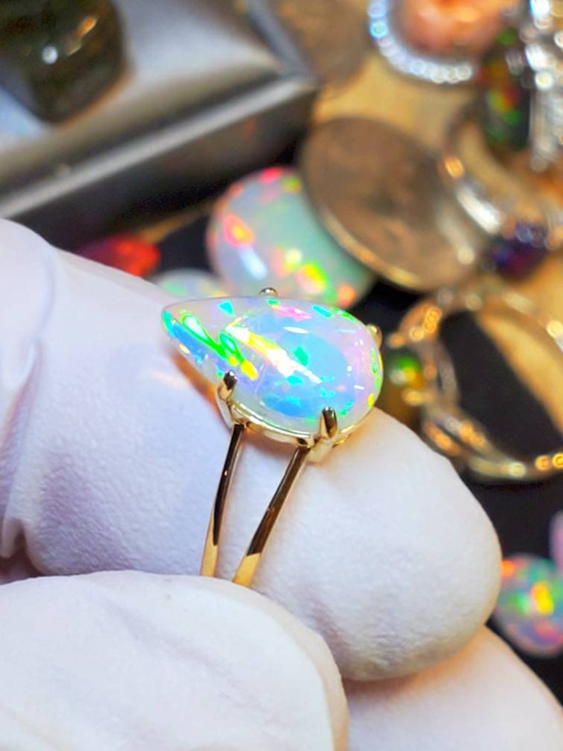 May include: A gold ring with a pear-shaped opal gemstone. The opal is iridescent with shades of green, blue, and pink.