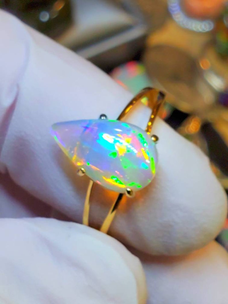 May include: A gold ring with a pear-shaped opal gemstone. The opal is iridescent with shades of green, blue, and pink.