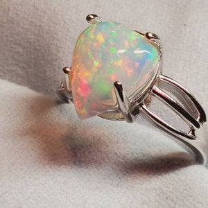 Pode incluir: Um anel de prata com uma grande pedra de opala em forma de p&ecirc;ra. O opala &eacute; iridescente com flashes de verde, azul e rosa.
