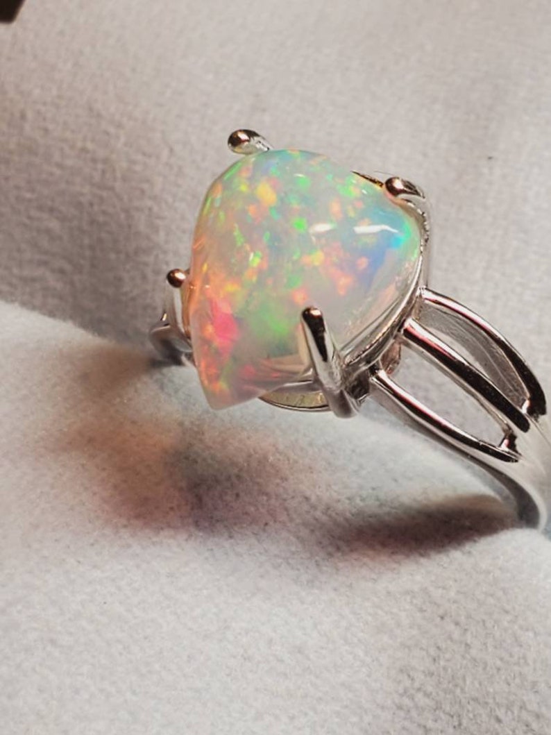 Pode incluir: Um anel de prata com uma grande pedra de opala em forma de p&ecirc;ra. O opala &eacute; iridescente com flashes de verde, azul e rosa.