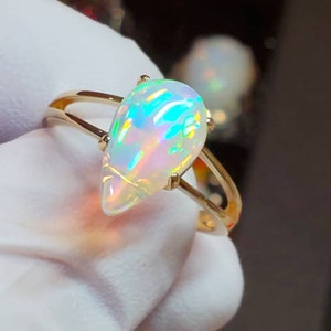 May include: A gold ring with a teardrop-shaped opal gemstone. The opal is iridescent with flashes of green, blue, and pink.