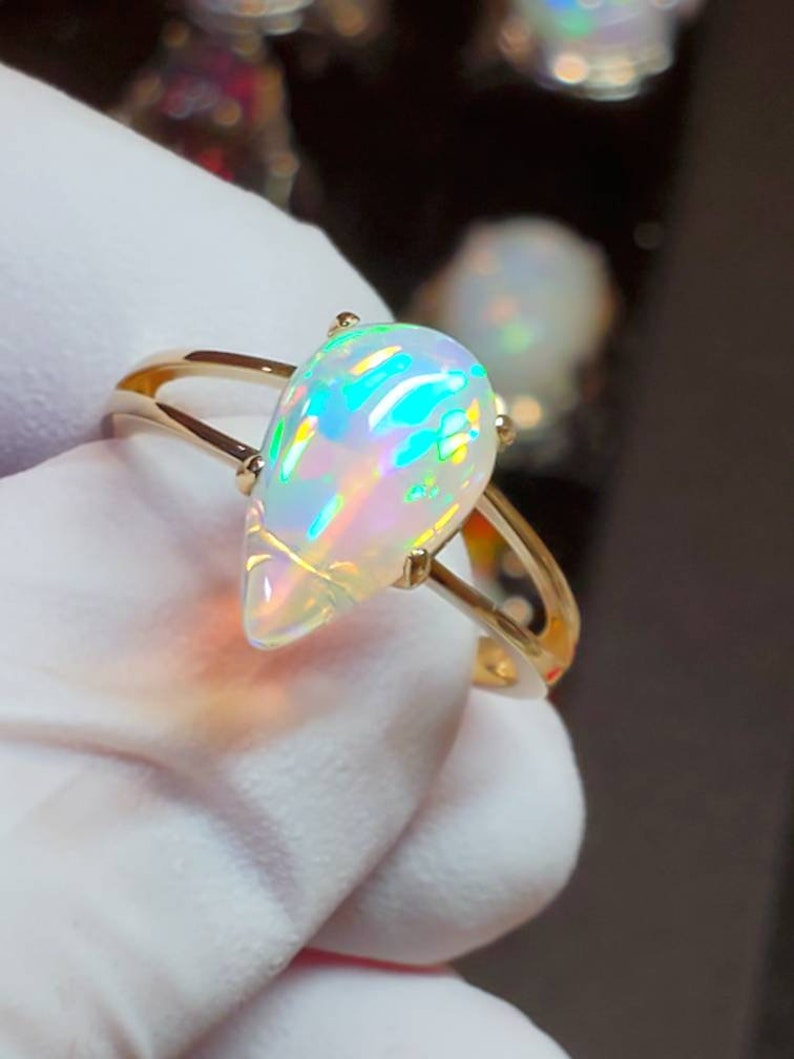 May include: A gold ring with a teardrop-shaped opal gemstone. The opal is iridescent with flashes of green, blue, and pink.