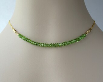 May include: A delicate gold chain necklace with a row of small, green peridot beads.