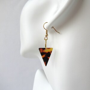 May include: Gold tone triangle earrings with a brown and black tortoiseshell pattern.