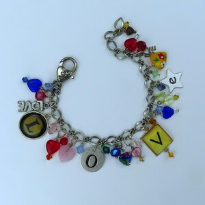 May include: A silver charm bracelet with a variety of charms, including hearts, stars, letters, and beads. The charms are in various colors, including red, blue, yellow, and green. The bracelet is made of a silver chain and has a lobster clasp.