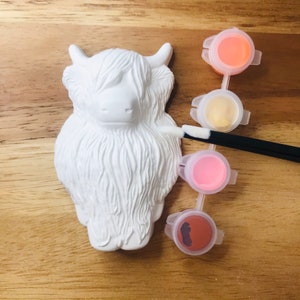 May include: White ceramic Highland Cow figurine with a paintbrush and four small paint pots in orange, yellow, pink, and brown.