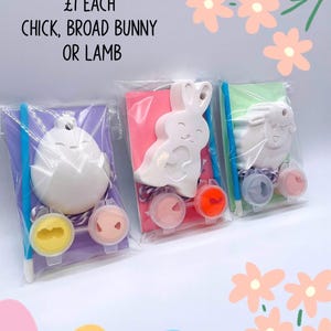 May include: Three paint-your-own Easter-themed kits: a chick, a bunny, and a lamb. Each kit includes a plaster figure, paint pots, and a paintbrush, all packaged in clear plastic. The text "FIVER FRIDAY" and "CHICK, BROAD BUNNY OR LAMB" is visible.