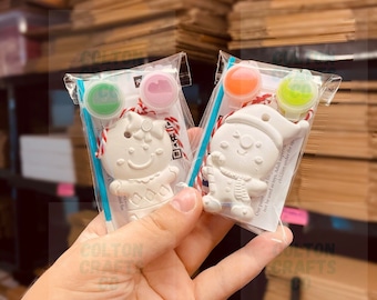 May include: Two paint-your-own Christmas ornaments in clear plastic bags. One is a gingerbread person, the other a snowman. Each kit includes paint pots in pink, green, orange, and yellow, plus a paintbrush and string.