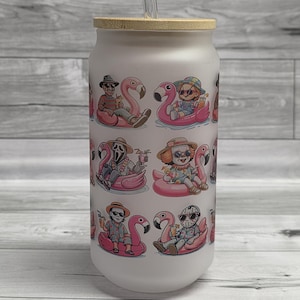 May include: A white glass can-shaped tumbler with a bamboo lid and clear straw. The tumbler features a repeating pattern of cartoon characters on pink flamingo floats. The characters are wearing sunglasses and hats. A fun, summer-themed drinkware item.