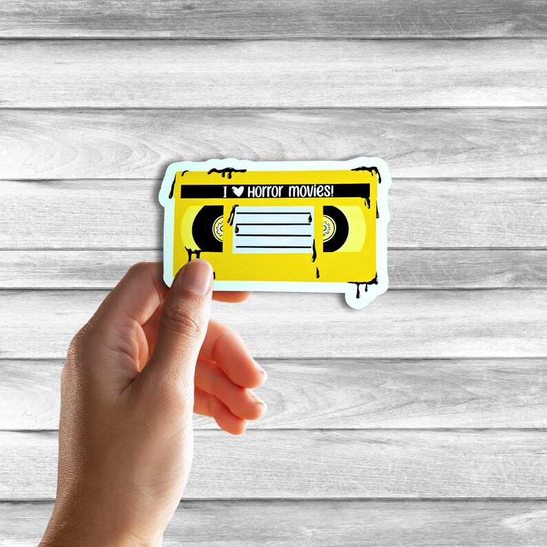 May include: Yellow VHS tape sticker with black dripping paint. The tape has a heart and the text "I &hearts; horror movies!" on the label.