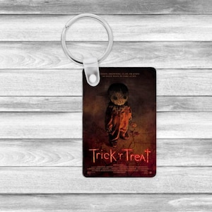 May include: A rectangular keychain featuring a horror movie poster design. The keychain has a silver metal ring and a printed image of a character from the movie "Trick 'r Treat". The title is in red, and the background is dark.