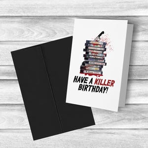 May include: A white card with a stack of VHS tapes with a bloody knife sticking out of the top. The text on the card reads "Have a Killer Birthday!"