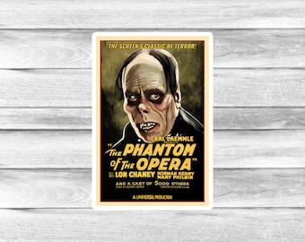 May include: A sticker featuring a vintage movie poster for "The Phantom of the Opera." The poster has a dark color scheme with the title in bold, stylized lettering. The image includes a portrait of the Phantom.