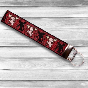 May include: Red keychain with a repeating pattern of a small, pink, cartoon creature with black eyes and a black shadow. The keychain has a silver metal ring.