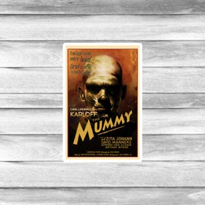 May include: A vintage movie poster for "The Mummy" featuring a close-up of the mummy's face with wrapped bandages. The poster has a dark color scheme with text that reads "From Egypt's ancient sands he awakes!" and the names of the actors.