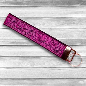 May include: A pink key chain with a black spider web design and a gold metal key ring.