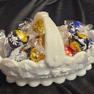 Peut inclure: Un panier en porcelaine blanche avec une poignée, rempli de truffes au chocolat assorties enveloppées de papier d'aluminium doré et argenté. Les truffes sont étiquetées "70% Cacao".