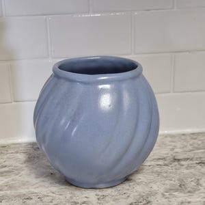 May include: A light blue ceramic vase with a swirled design. The vase is round and has a wide opening.
