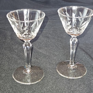 May include: Two clear glass stemmed drinking glasses with etched leaf designs.