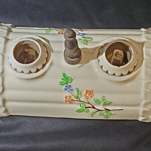 May include: A white ceramic light fixture with two sockets and a floral design. The fixture has a decorative wooden knob on top.