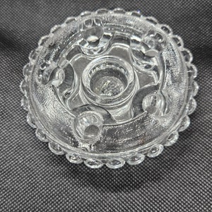 May include: A clear glass candle holder with a beaded edge and five candle cups. The holder has a decorative design with a central cup and four smaller cups around it.