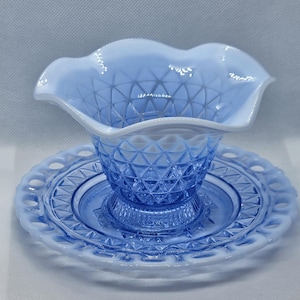 May include: A light blue glass dish set with a ruffled edge bowl and a matching saucer. The bowl and saucer have a diamond pattern design. The edges of the bowl and saucer are white.