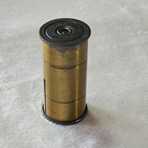 May include: A brass film canister with a black top. The top has a small hole in the center.