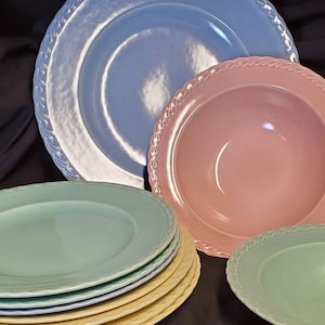 May include: A set of pastel-colored ceramic plates and bowls. The set includes a large blue plate, a pink bowl, a stack of four smaller plates in shades of yellow, blue, and green, and a green bowl.