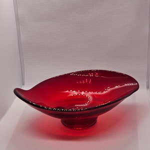 Puede incluir: Un cuenco de vidrio rojo oscuro con un borde ondulado y una base de pedestal. El cuenco está hecho de vidrio transparente con un tinte rojo.