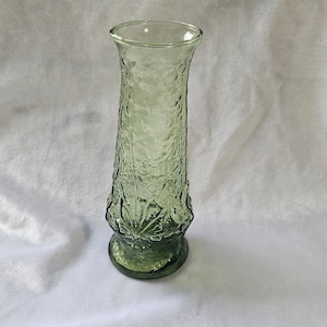 May include: A green glass vase with a textured surface. The vase has a wide base and a narrow neck.
