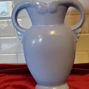 May include: A light blue ceramic vase with two handles. The vase has a rounded body and a flared top.