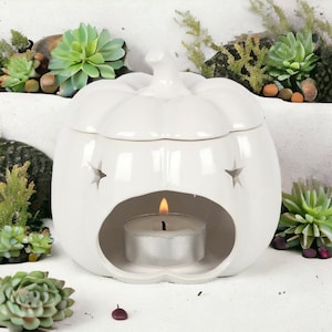 Könnte beinhalten: Weißer, keramik-geformter Kürbis-Wachs-Schmelzofen mit einem Stern-Ausschnitt-Design. Eine kleine Teelichtkerze wird in den Schmelzofen gestellt.