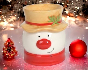 May include: A white ceramic snowman wax warmer with a red scarf, red nose, and a brown hat with a green leaf.