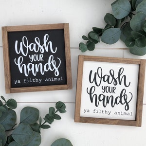 May include: Two wooden signs with the text "Wash your hands ya filthy animal" in white lettering on a black background and black lettering on a white background.