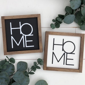 May include: Two wooden framed signs with the word "HOME" in black and white lettering. The sign on the left has a black background and white lettering. The sign on the right has a white background and black lettering.