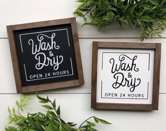 May include: Two wooden signs with the text "Wash & Dry Open 24 Hours" in white lettering. One sign has a black background and the other has a white background.