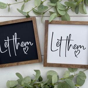May include: Two wooden framed signs with the text "Let them" and a heart symbol. One sign has a black background with white text and the other has a white background with black text.