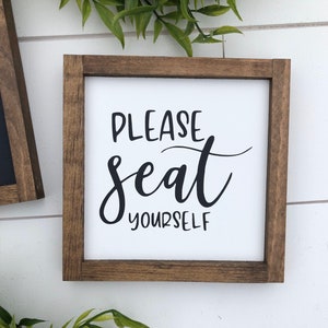 May include: A wooden framed sign with white background and black text that reads "Please seat yourself".