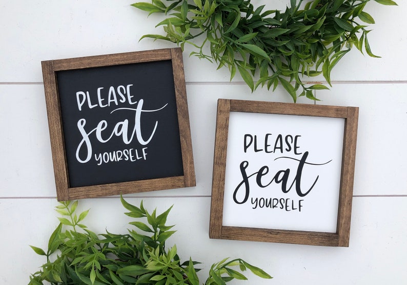 May include: Two wooden signs with the text "Please seat yourself" in black and white lettering. The signs are framed in brown wood and have a rustic look.