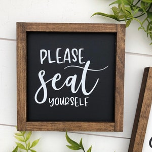May include: A wooden framed sign with a black background and white text that reads "Please seat yourself".