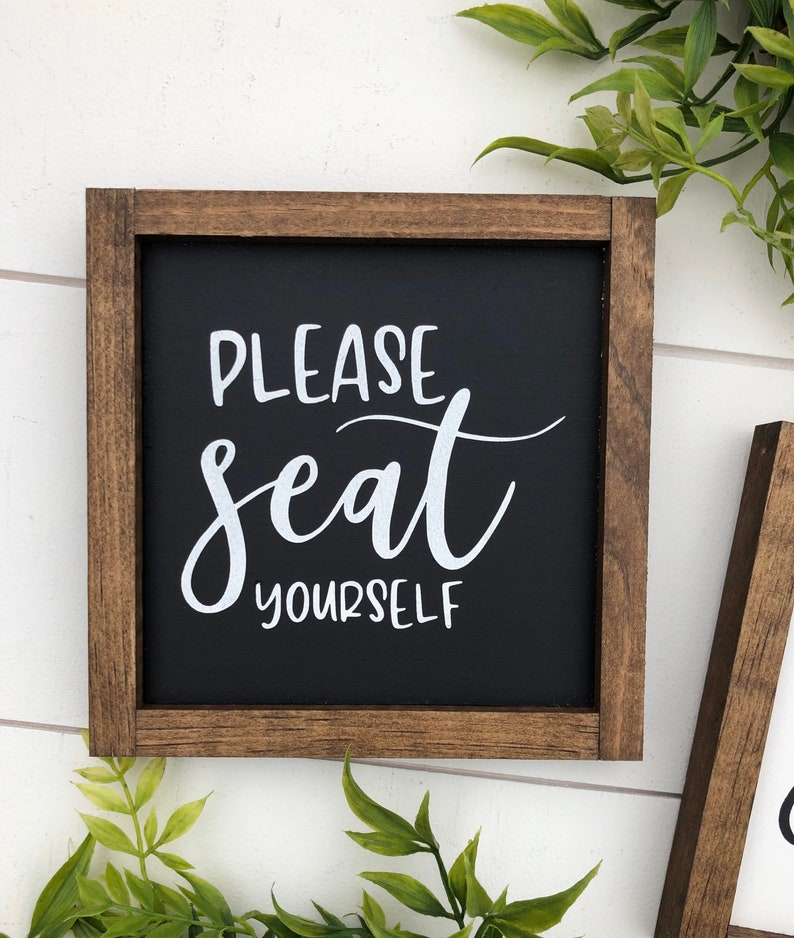 May include: A wooden framed sign with a black background and white text that reads "Please seat yourself".