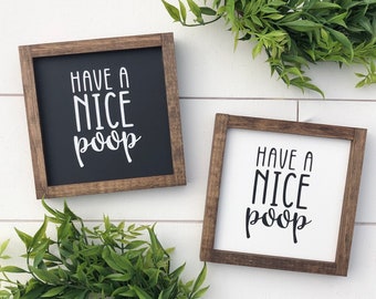 May include: Two wooden framed signs with the text "Have a Nice Poop" in white lettering. The signs are on a white background.