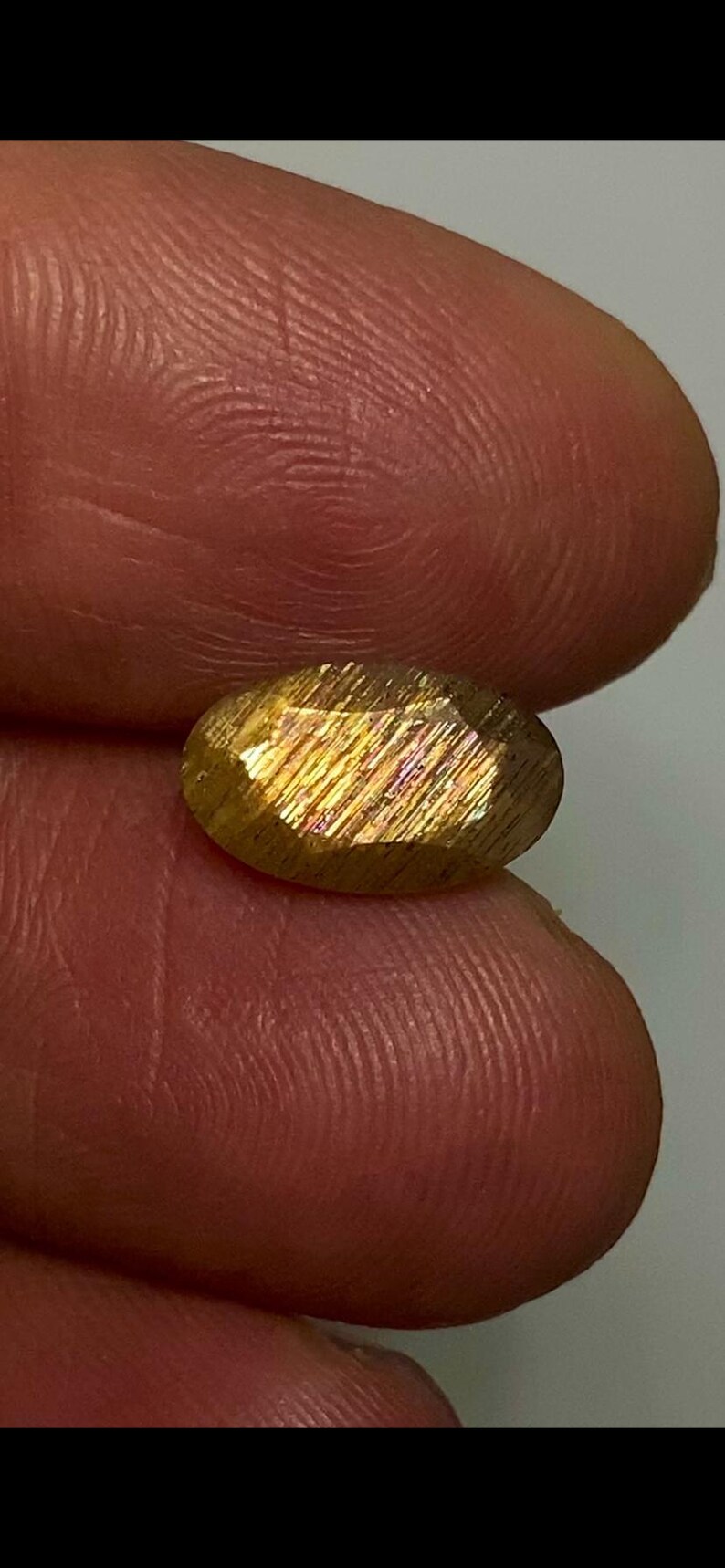 May include: An oval-shaped sunstone gemstone featuring a faceted surface with a golden-brown hue and internal reflective metallic inclusions that create a shimmering effect when light hits the stone's polished, multi-faceted exterior surface.