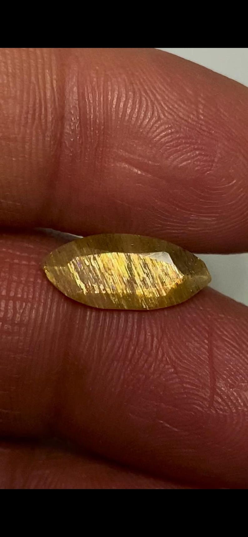 May include: A marquise-cut sunstone gemstone featuring a translucent golden-brown hue with internal metallic copper-coloured inclusions that create a shimmering aventurescence effect across the faceted surface of the stone.