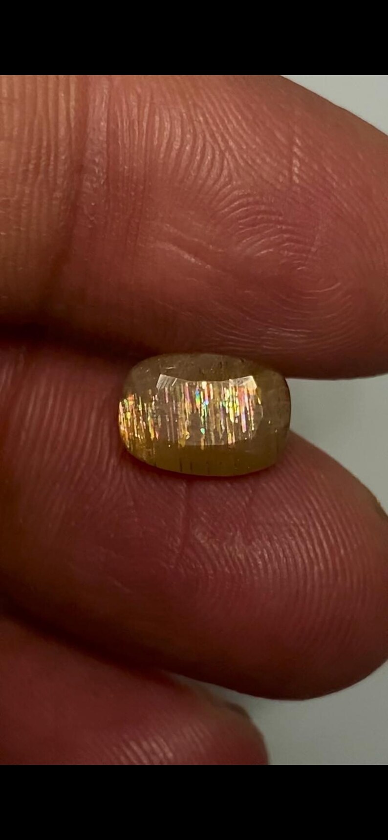 May include: A faceted oval sunstone gemstone featuring a translucent golden-brown base colour with internal metallic inclusions that create a distinct shimmering aventurescence effect with flashes of rainbow colours across the surface of the stone.