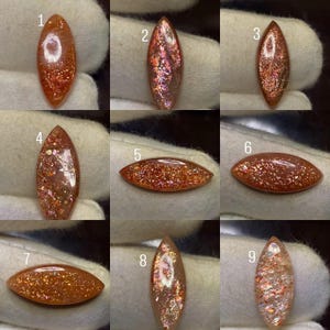 Puede incluir: Una colección de nueve piedras preciosas de piedra solar con corte marquesa, numeradas del uno al nueve. Cada piedra muestra un color base único naranja, melocotón o claro con inclusiones metálicas brillantes que varían en densidad.