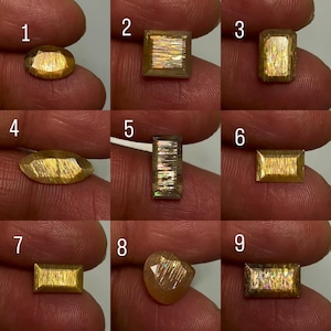 May include: A collection of nine faceted sunstone gemstones in various shapes including oval, square, rectangular, and marquise cuts. Each stone displays a golden-brown hue with internal metallic aventurescence and shimmering light reflections.