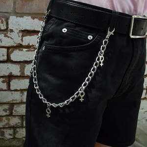 May include: A silver chain with multiple charms in the shape of the female symbol. The chain is attached to a black belt worn around a person's waist.