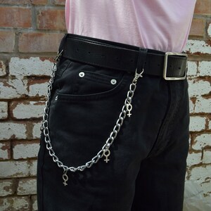 May include: A silver chain with female symbols hanging from a black belt worn over black shorts.